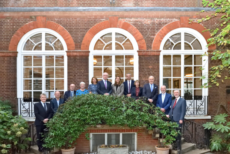 Leaders of AHSC member organisations standing on steps outside a redbrick building with large windows.